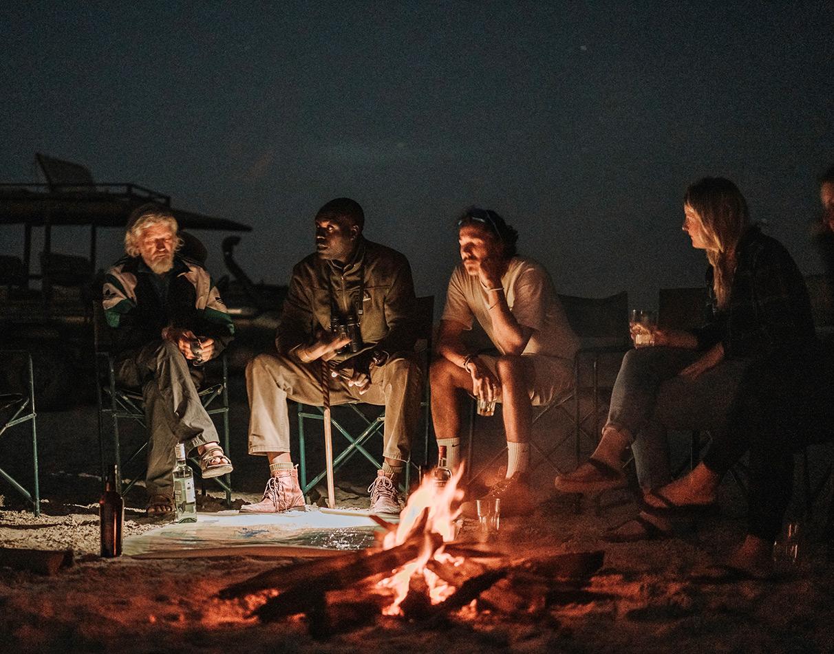 A group of self-drive travellers sitting around a campfire at night.