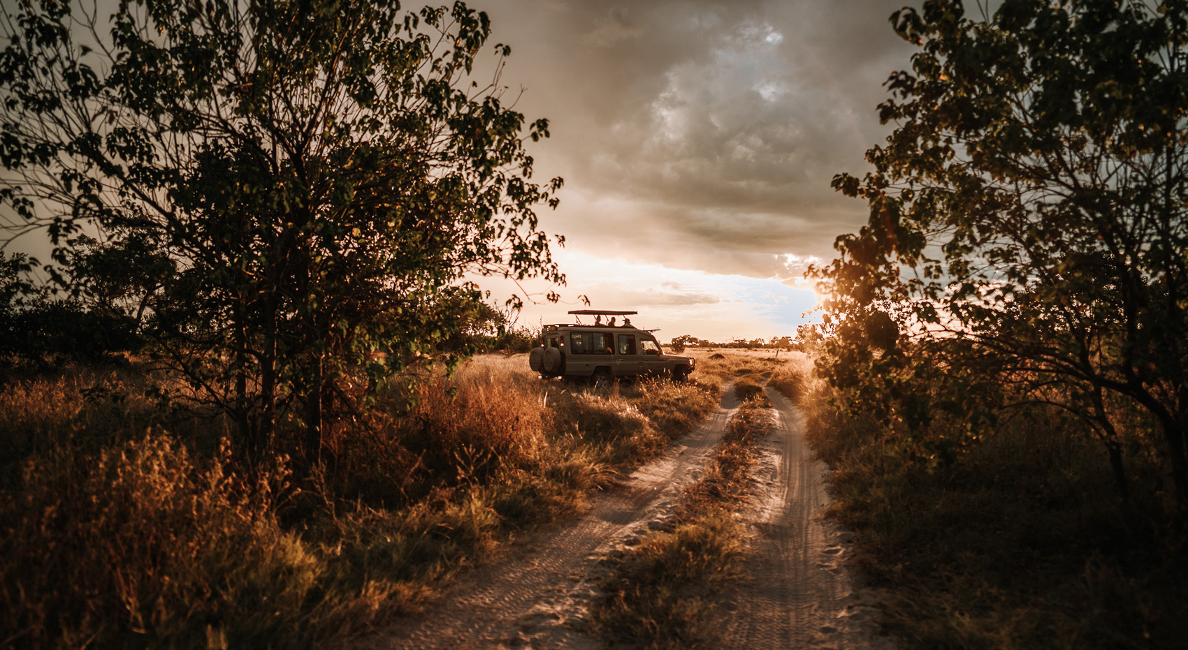 Ein Sonnenuntergang in Botswana mit einem Safarifahrzeug und Gästen, die über die Ebenen blicken. 