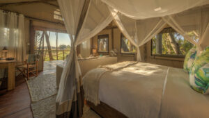 A four-poster bed with mosquito nets faces the view of the wild in one of Setari Camps' spacious bedrooms.