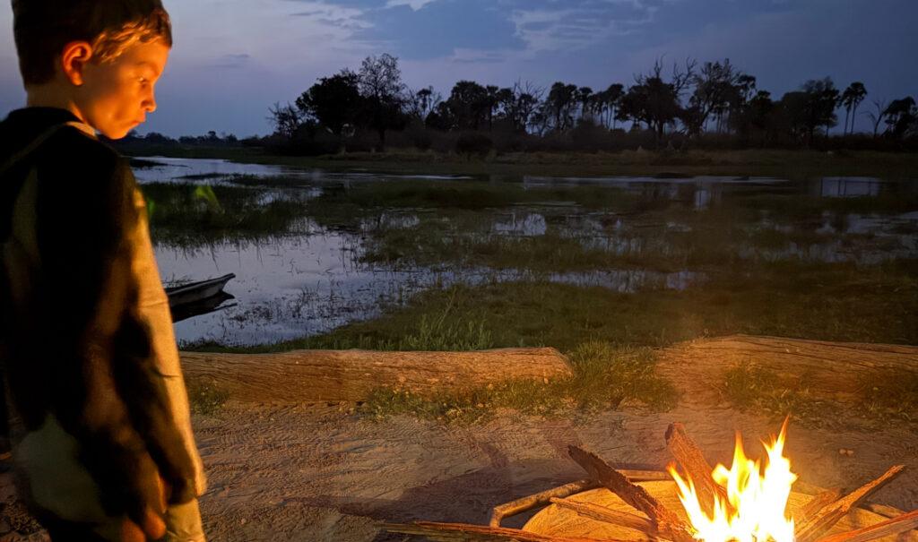 A young boy watching a fire while camping in Botswana.